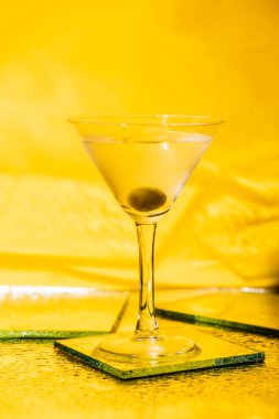 green olive in glass with martini on yellow  clipart