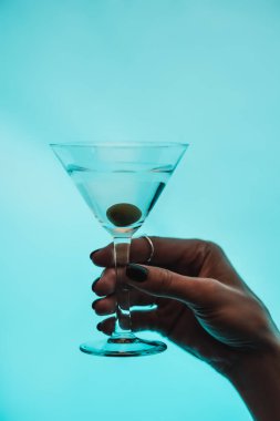 Kırpılmış bir kadın elinde bir bardak martini tutarken mavi zeytinli.