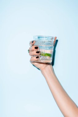 cropped view of woman holding glass with lime in alcohol drink on blue clipart