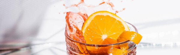 orange peel in glass with splashed alcohol cocktail on white, banner