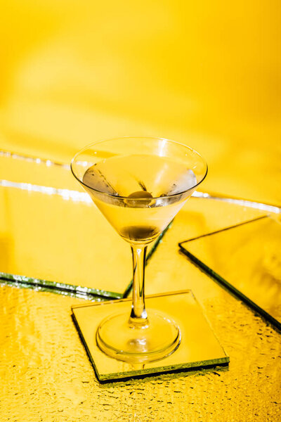 green olive in glass of martini on yellow 