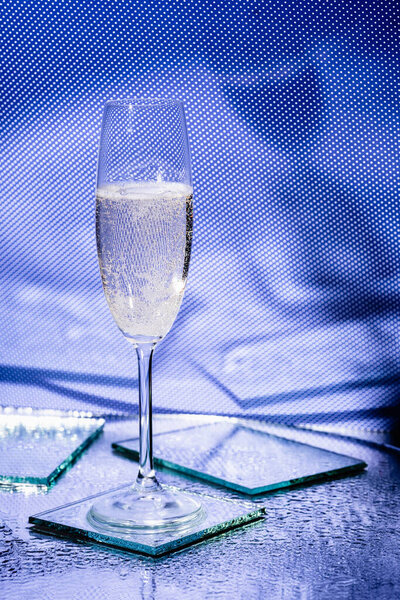 glass of champagne near mirrors on surface and blue background