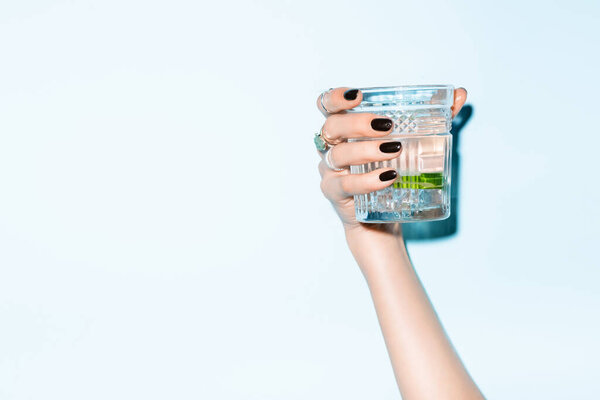 cropped view of young woman holding glass with lime in alcohol drink on blue