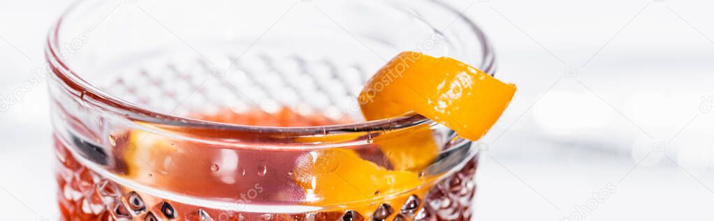 orange peel in glass with alcohol cocktail on white, banner