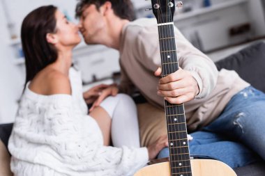 Bulanık arka planda bir adamın sevgilisini öptüğü akustik gitar. 
