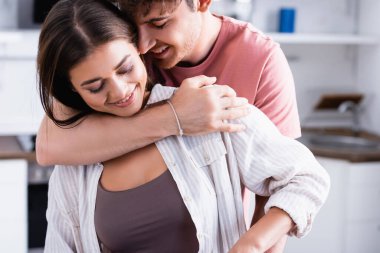 Mutfakta gülümseyen kadına sarılan adam. 