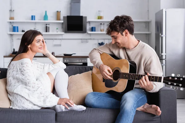 Mujer Sonriente Sentada Cerca Novio Tocando Guitarra Acústica Casa — Foto de Stock