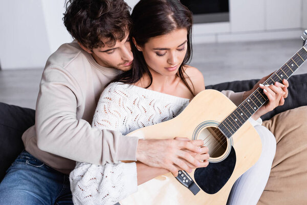 Young couple playing acoustic guitar on sofa together 