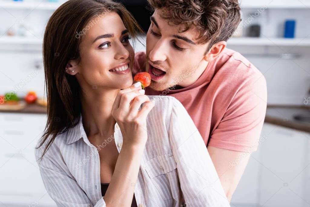 Smiling woman feeding boyfriend with fresh strawberry at home 