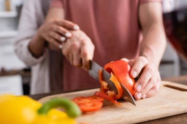 Kırpılmış erkek görüntüsü bulanık arka planda kız arkadaşının yanında kırmızı biber kesiyor. 