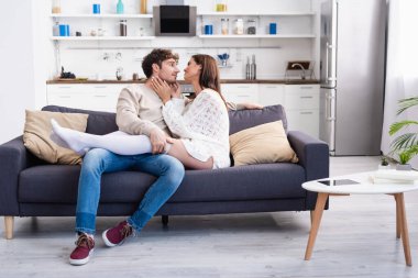 Dijital tabletin yanındaki kanepede erkek arkadaşına dokunan genç bir kadın ve sehpanın üzerindeki kitaplar. 