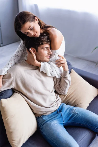 Mujer Morena Abrazando Novio Sonriente Sofá Con Almohadas Casa — Foto de Stock