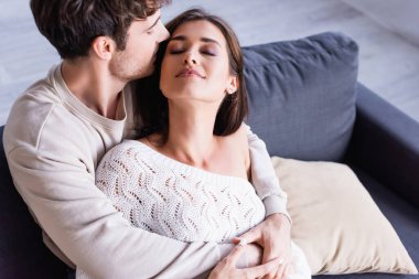 Genç adam kanepede esmer kız arkadaşını öpüyor. 