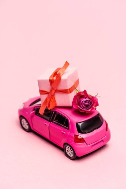 Oyuncak araba ve pembe arka planlı hediye kutusu.