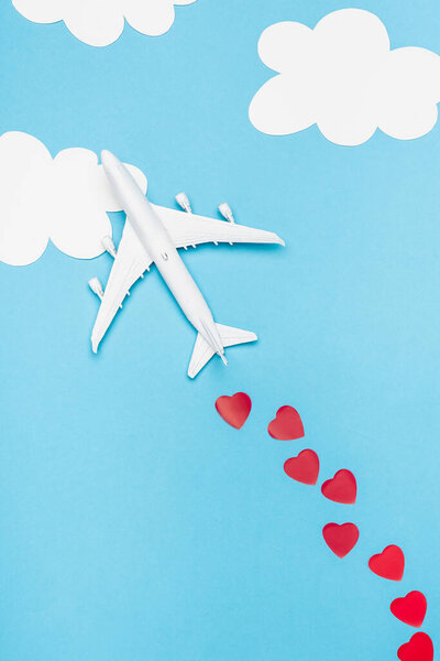 top view of plane model and red hearts on blue background with white clouds