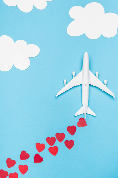 top view of plane model and red hearts on blue background with white clouds
