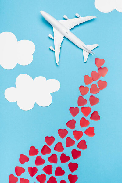 top view of plane model and red hearts on blue background with white clouds