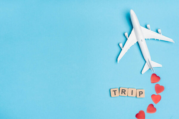 top view of plane model, word trip and red hearts on blue background