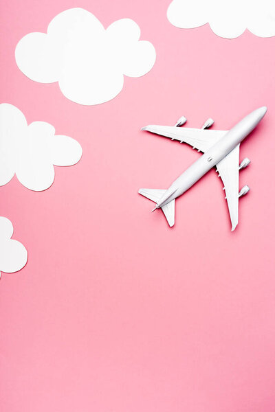top view of white plane model on pink background with clouds