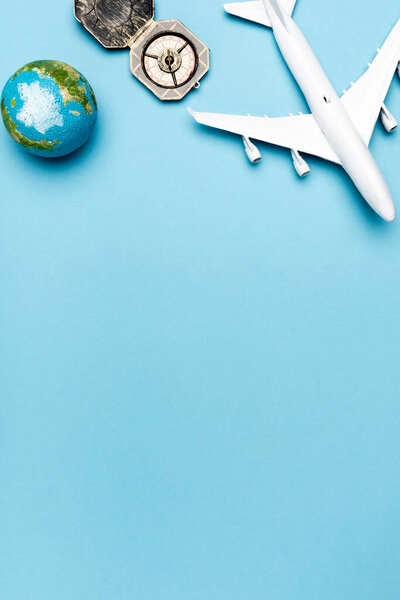 top view of white plane model, compass, globe on blue background