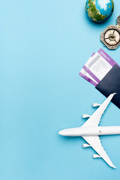 top view of white plane model, compass, globe and tickets on blue background