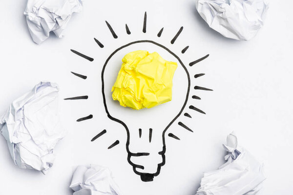 top view of light bulb with crumpled papers on white background