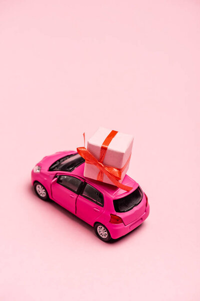 игрушечный автомобиль и подарочная коробка на розовом фоне