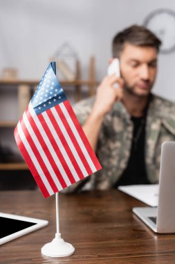 Amerikan bayrağı ve dijital tableti bulanık arka planda üniformalı askerin yanında.