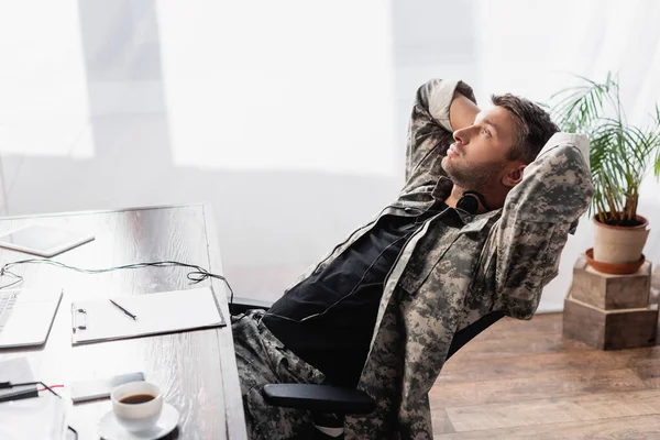 soldier in military uniform and headset resting near gadgets on chair