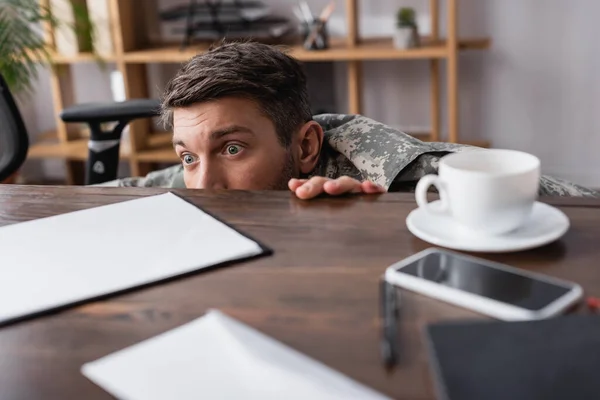 Φοβισμένος Στρατιωτικός Κρύβεται Κάτω Από Γραφείο Φλιτζάνι Καφέ Και Smartphone — Φωτογραφία Αρχείου