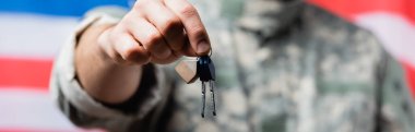 partial view of patriotic military man holding keys near american flag on blurred background clipart