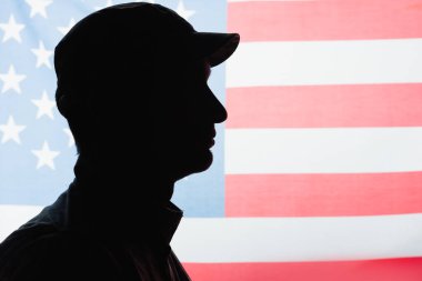 Arka planda Amerikan bayrağı yanında üniformalı ve şapkalı vatansever bir askerin yan görünüşü