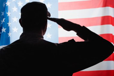 back view of patriotic military man in uniform and cap giving salute near american flag  clipart