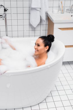 Küvette köpükle banyo yapan neşeli genç bir kadın. 