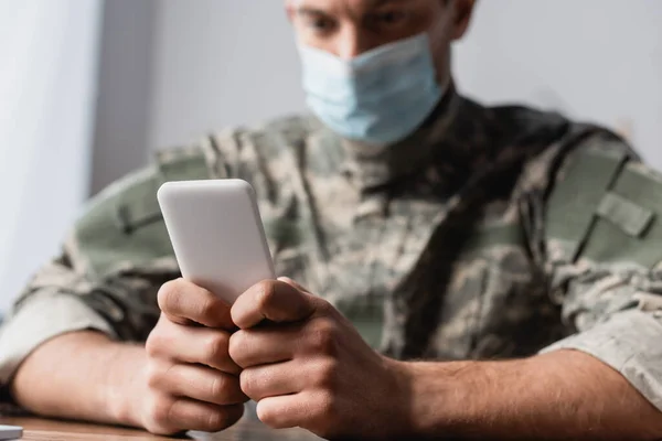 手持智能手机的军人身穿制服 医疗面具的背景模糊不清 — 图库照片