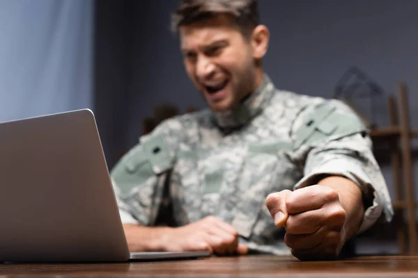 愤怒的军人 身穿制服 紧握拳头坐在笔记本电脑旁 背景模糊不清 — 图库照片