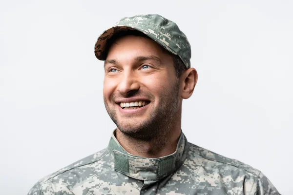 happy military man in uniform and cap looking away isolated on white