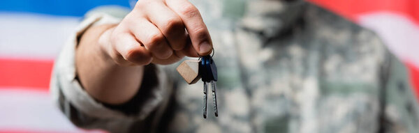 partial view of patriotic military man holding keys near american flag on blurred background
