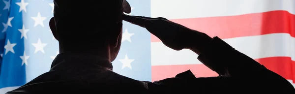 制服を着た愛国的な軍人がアメリカ国旗の近くで敬礼をする姿を — ストック写真
