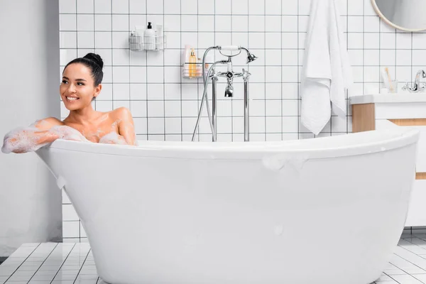 Positive Brunette Woman Looking Away While Sitting Bathtub Foam — Stock Photo, Image