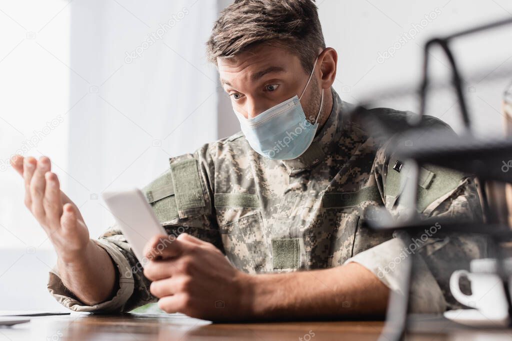 military man in uniform and medical mask using smartphone near documentary tray on blurred foreground