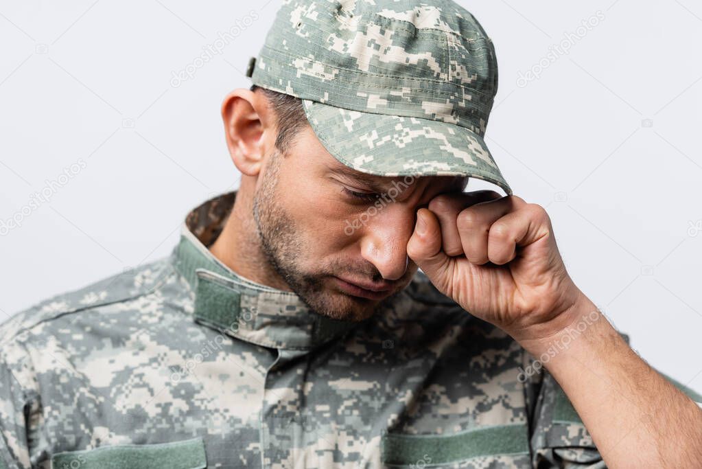 sad military man in uniform and cap wiping tears while crying isolated on white