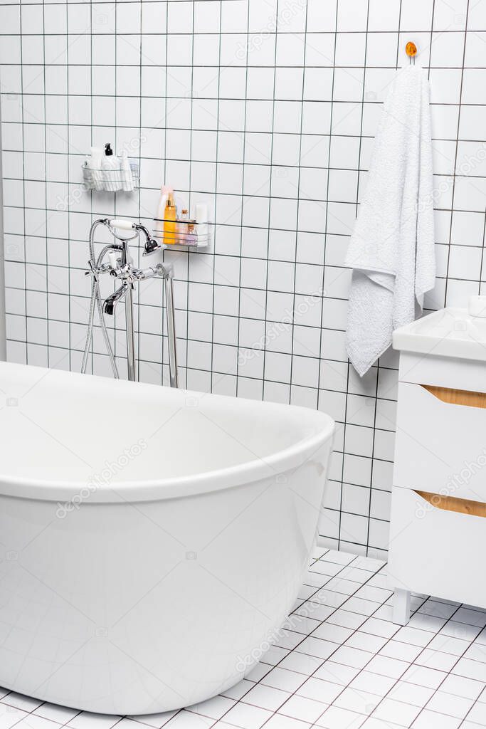 Toiletries near towel and bathtub in modern white bathroom 