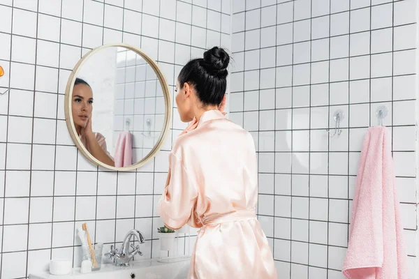 Jonge Vrouw Satijn Badjas Aanraken Huid Buurt Spiegel Badkamer — Stockfoto