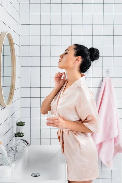 Jovem Mulher Roupão Banho Seda Aplicando Soro Cosmético Perto Espelho — Fotografia de Stock