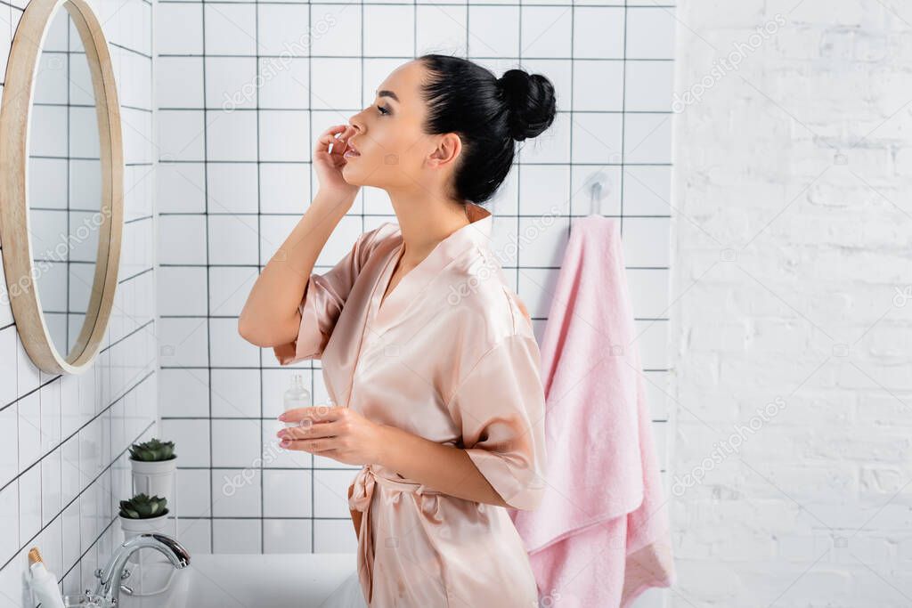 Young woman applying cosmetic serum near mirror in bathroom 