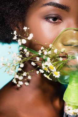 Mavi arka planda solunum cihazında çiçekleri olan Afrikalı Amerikalı genç bir kadının yakın çekimi.