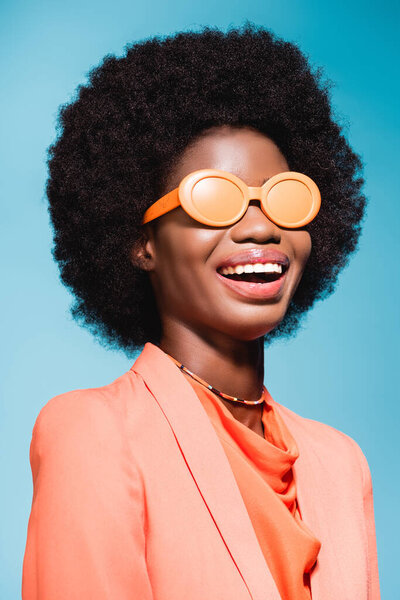 happy african american young woman in orange stylish outfit isolated on blue background