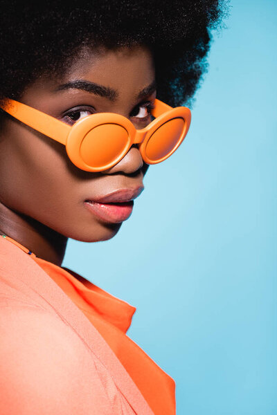 african american young woman in orange stylish outfit isolated on blue background