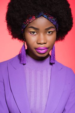Kırmızı arka planda izole edilmiş mor giysili Afro-Amerikan genç kadın.